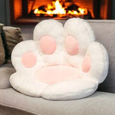 a cat paw pillow sitting on top of a couch next to a fire burning in the fireplace