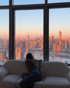 a woman sitting on top of a couch in front of a window looking out at the city