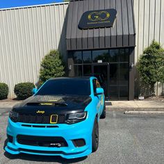 a blue and black car parked in front of a building with its hood up on