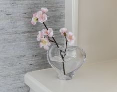 a glass vase with pink flowers in it on a white shelf next to a wall