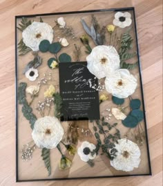 a black and white wedding card surrounded by flowers on a wooden floor with greenery