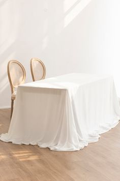 two chairs and a table with a white cloth draped over it in an empty room