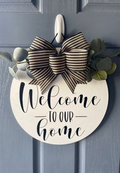 a welcome sign hanging on the front door with a bow and eucalyptus leaves around it