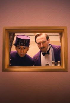 two men in tuxedos are looking at the camera through a gold framed mirror