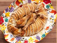 a platter with sliced chicken on it and colorful flowers around the edges, sitting on a wooden table