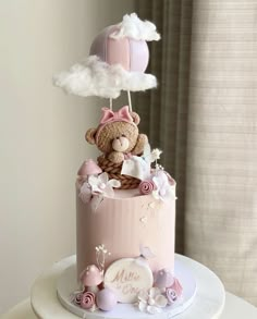 a teddy bear is sitting on top of a pink cake with white clouds and flowers