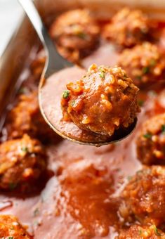 a spoon full of meatballs with sauce and parmesan cheese on the side