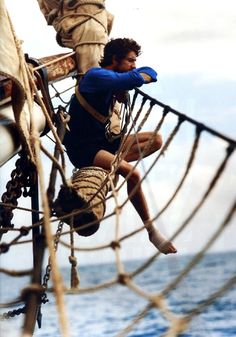 a man climbing up the side of a tall ship in the ocean with ropes on both sides