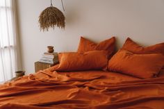 a bed with orange sheets and pillows on top of it next to a plant hanging from the wall