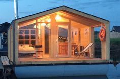 a boathouse is lit up at night on the water with chairs and a table