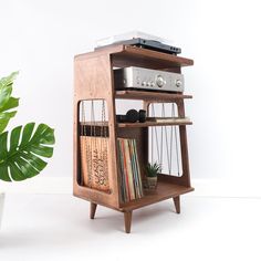 a wooden shelf with books, record player and plant in it next to a white wall