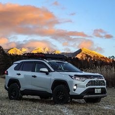 a white toyota rav is parked in the grass with mountains in the background at sunset