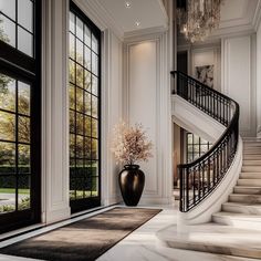 an elegant foyer with stairs, chandelier and large vase filled with flowers on the floor