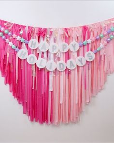 a happy birthday banner with pink, blue and white streamers hanging from the wall