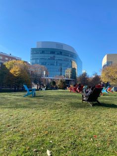 people are sitting in chairs on the grass near a large glass building with many windows