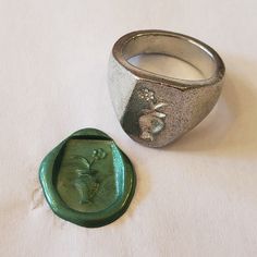 a wax stamp next to a silver ring on a white tablecloth with a flower design