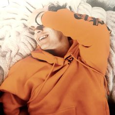 a man laying on top of a bed wearing an orange hoodie and smiling at the camera