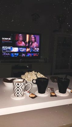 a table topped with cups and bowls filled with food next to a flat screen tv