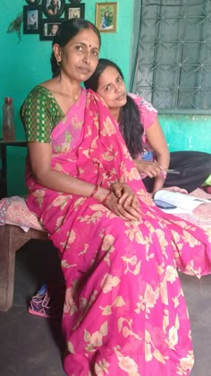 two women in pink sari sitting next to each other on a bed with green walls