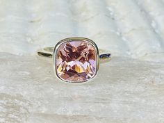 a ring with a pink stone in the center on a marble slab, sitting on top of a rock