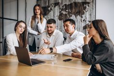 a group of people sitting around a wooden table in front of laptops and papers