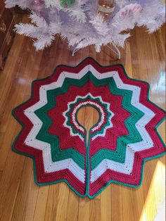 a crocheted christmas tree skirt sitting on the floor next to a pink and white tree