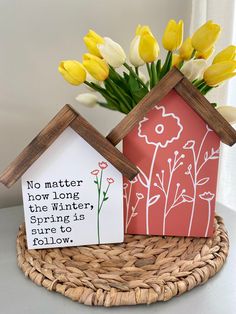 two small houses sitting on top of a wicker basket filled with yellow and white flowers