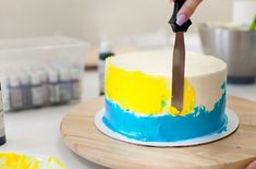 a person cutting a cake with a knife on a wooden board next to some paint