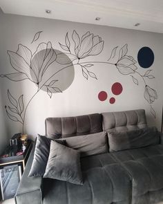 a grey couch sitting in front of a wall with flowers painted on it's side