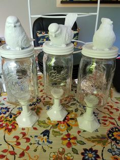 three glass jars sitting on top of a table covered in white frosting and birds