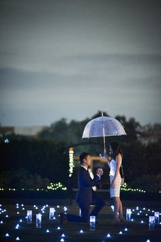 a man kneeling down next to a woman holding an umbrella in front of some lights