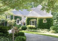 a house covered in ivy with a mailbox on the sidewalk and trees around it