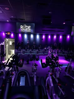 an indoor gym with purple lighting and rows of exercise bikes