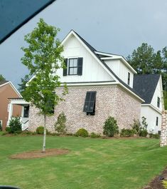 a white house with black shutters and trees in the front yard on a cloudy day