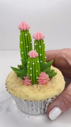 a hand holding a cupcake decorated with pink flowers and green cactus on it's top