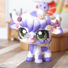 a small toy cow with big eyes and flowers on it's head sitting on a wooden table