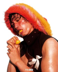 a man with an orange and yellow mohawk on his head is eating something while wearing a black shirt