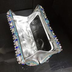 a silver case with blue and white beads on it sitting on a black table next to a cell phone