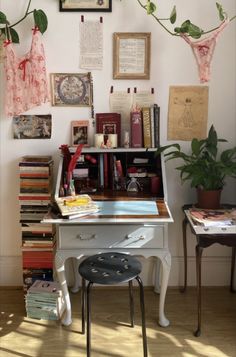 a white desk topped with lots of books next to a wall covered in pictures and plants