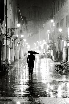 a person with an umbrella walks down the street in the rain at night, on a rainy day