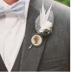 a man wearing a gray suit and bow tie with a white feather brooch on his lapel