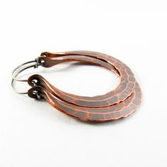 "Our medium large hammered copper Rio hoop earrings are earthy, rustic and beautiful, hand forged from large 10 gauge copper wire and oxidized for a deep glow. Fitted with standard 20 gauge sterling silver ear wires. Perfect for a weekend in Rio or anywhere an edgy punch to your wardrobe is needed! A great 7th anniversary jewelry gift. Earrings measure a touch under 2\" or 5.08cm long and 1.5\" or 3.81cm wide NOTE: Made To Order - Please Allow 3-5 business days for completion. The beauty of hand Artisan Bronze Copper Hoop Earrings, Rust Colored Hammered Copper Jewelry, Hoop Earrings Medium, Hoop Earrings Large, Rustic Earrings, Mixed Metal Earrings, 7th Anniversary, Anniversary Jewelry, Earrings Large