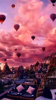 many hot air balloons are flying in the sky above some buildings and mountains at sunset