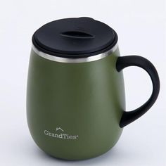 a green coffee mug with a black lid and handle sitting on a white table top