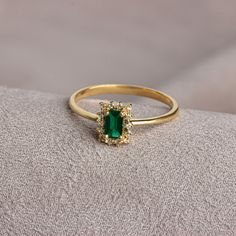 an emerald and diamond ring sitting on top of a pillow