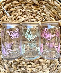 three glasses with butterfly designs on them sitting in front of a basket full of straw