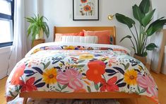 a bed with colorful flowers on it in a bedroom next to a potted plant