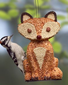 a bird feeder with a small bird on it's side and a fox decoration hanging from the top