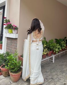 a woman in a white sari standing next to potted plants