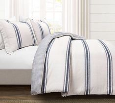 a bed with blue and white striped pillows on it's side, next to a window